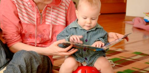 Child paging through a book with his mom while sitting on a potty